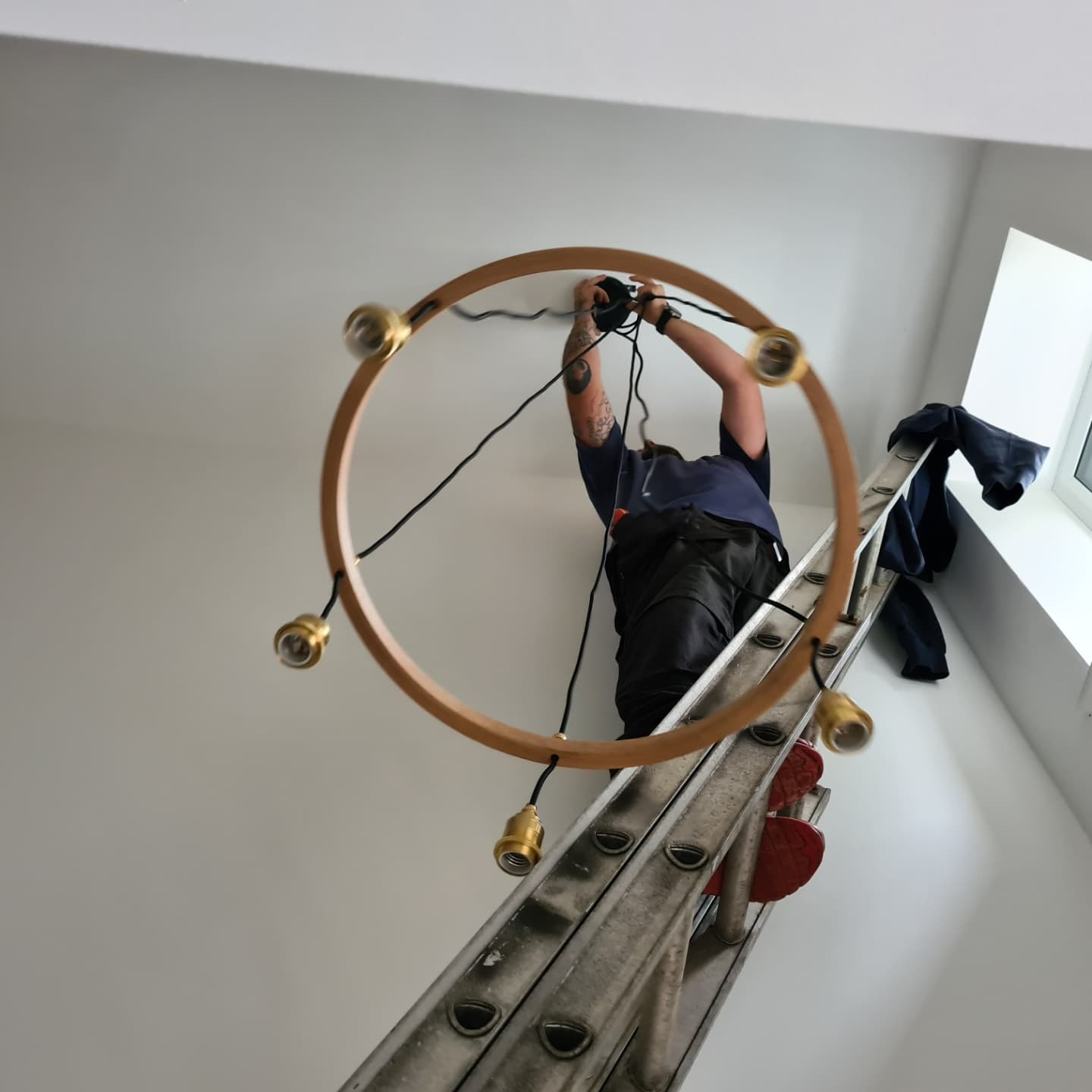 Electrician installing chandelier on ladder